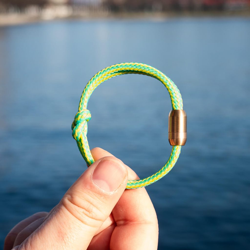 Ein Walvis Bay Armband von BRACENET wird in die Sonne gehalten. Es besteht aus grün-gelbem Fischernetz