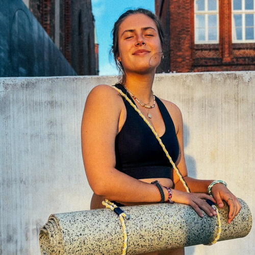 Hannah Nele steht mit dem von ihr und BRACENET entwickelten Tragegurt für Yogamatten im Sonnenuntergang