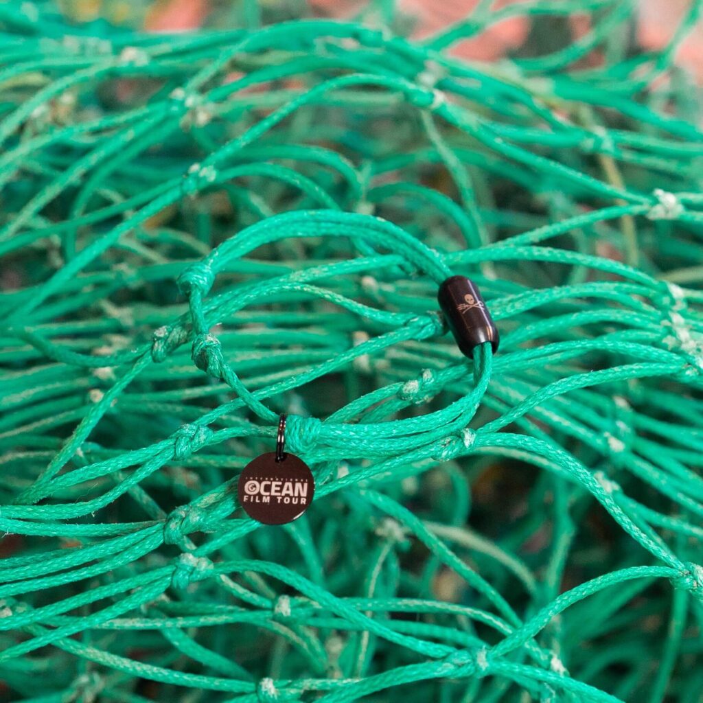 Grünes BRACENET Upcycling Armband mit schwarzem Edelstahlanhänger liegt auf altem Fischernetz
