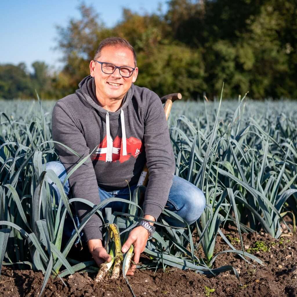 Uwe Wilms hockt mit grauem Hoodie und blauer Jeans in grünen Lauch-Feld, das mit BiOhumat gedüngt wurde