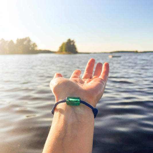 Person trägt das BRACENET Armband am Handgelenk, upgecycelt aus Fischernetzen mit Glasperle aus Schweden, im Hintergrund ein See