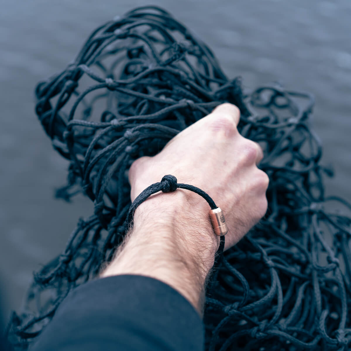 Schwarzes Fischernetz wird von Person gehalten, die ein BRACENET Upcycling Armband trägt.