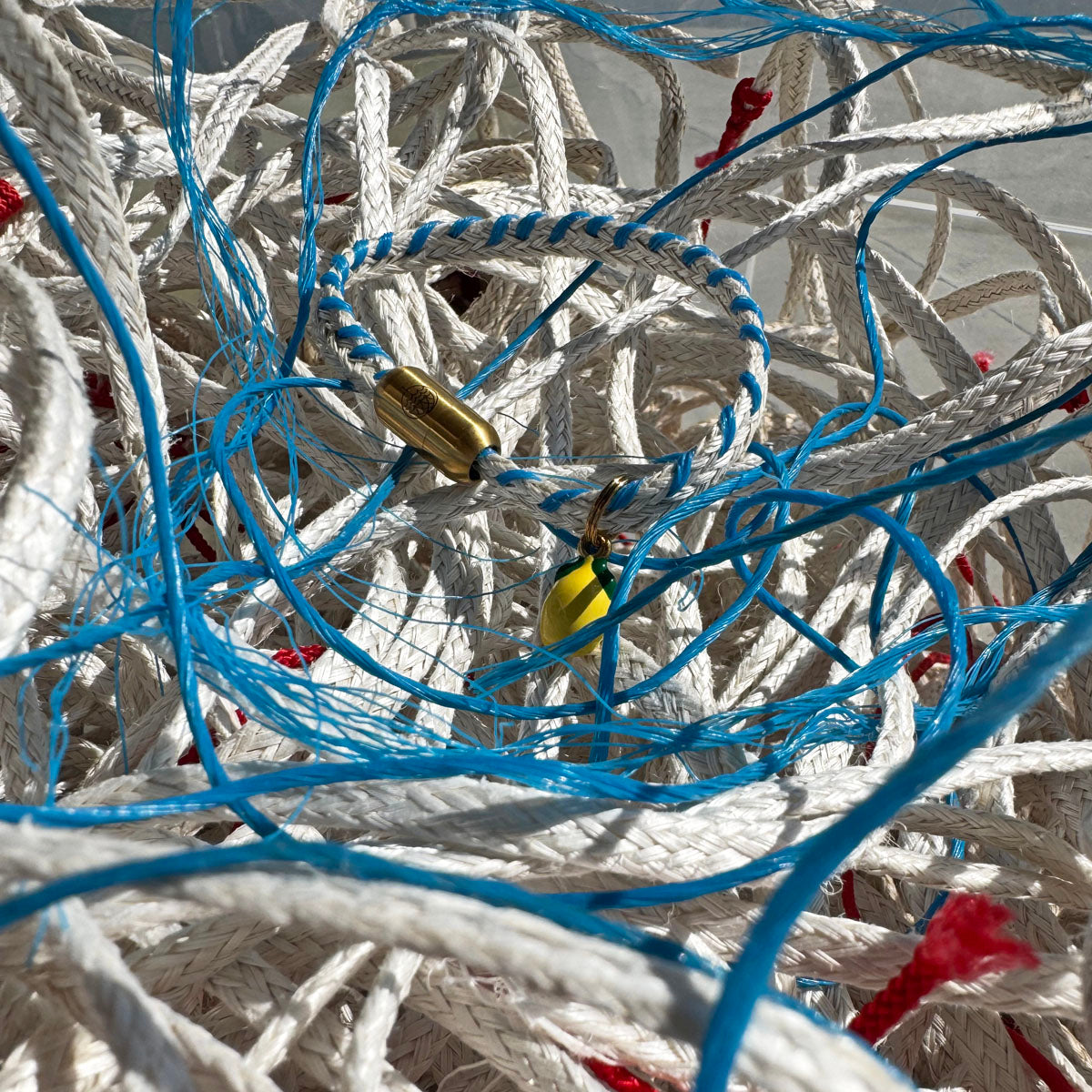 Almalfi Bracenet Bracelet aus Fischernetz in weiß und blau mit Edelstahl Magnetverschluss und einem Zitronenanhänger in der Hand mit Netzen Hintergrund