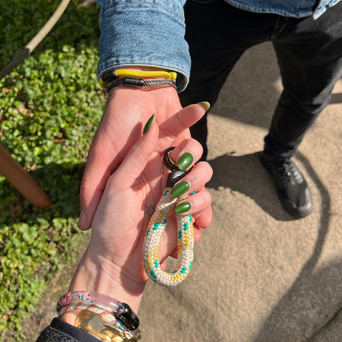 Zwei Personen halten Sea Shepherd X BRACENET x humanvoll Schlüsselanhänger mit schwarzer Kappe mit dem Sea Shepherd und humanvoll Logo aus weißem Fischereiseil mit gelben und grünen Akzenten sich an der Hand. Eine Person hält den Schlüsselanhänger in der Hand