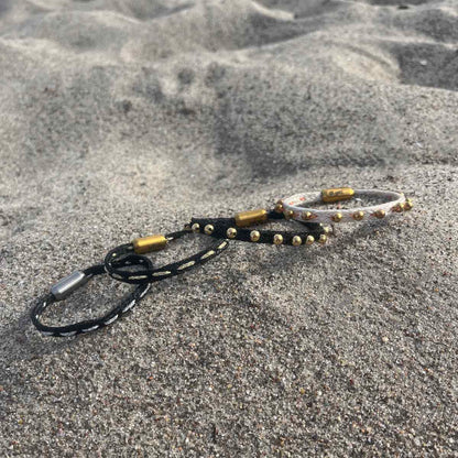 Alle Produkte der BRACENET Glam Edition liegen im Sand. Ganz rechts das Armband aus weißem Fischernetz mit goldenen Perlen und goldenem Magnet Verschluss. Daneben das Armband aus schwarzem Netz mit goldenen Perlen und goldenem Magnetverschluss. Daneben das Armband aus schwarzem Fischernetz mit goldenem Faden durchzogen und goldenem Magnetverschluss. Ganz links das Armband aus schwarzem Fischernetz mit silbernem Faden durchzogen und silbernem Magnetverschluss.