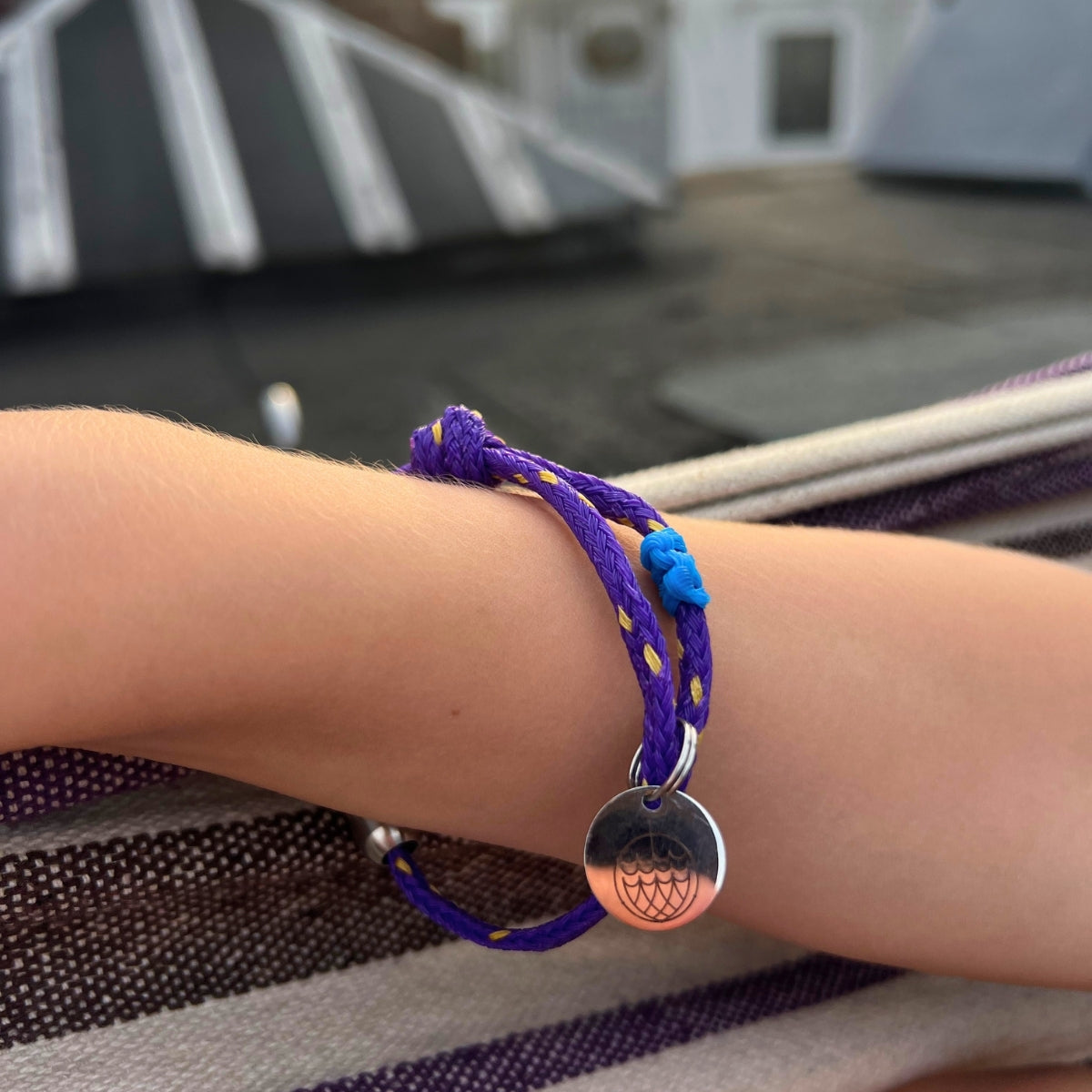 Kind trägt BRACENET Schulkind Bracenet aus Fischernetz in lila mit Makramee-Detil in Blau, Magnetverschluss in Silber und Anhänger in Silber mit Gravur ener Schultüte und der Aufschrift "Schulkind"