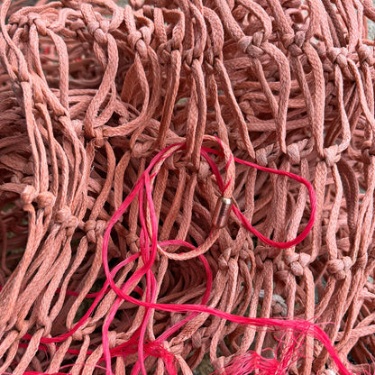 Februar Bracenet Amur Bay aus lachsfarbenen Fischernetz mit roten Dolly Ropes verziert und mit roségoldenen Magnetverschluss liegt auf Fischernetzen.