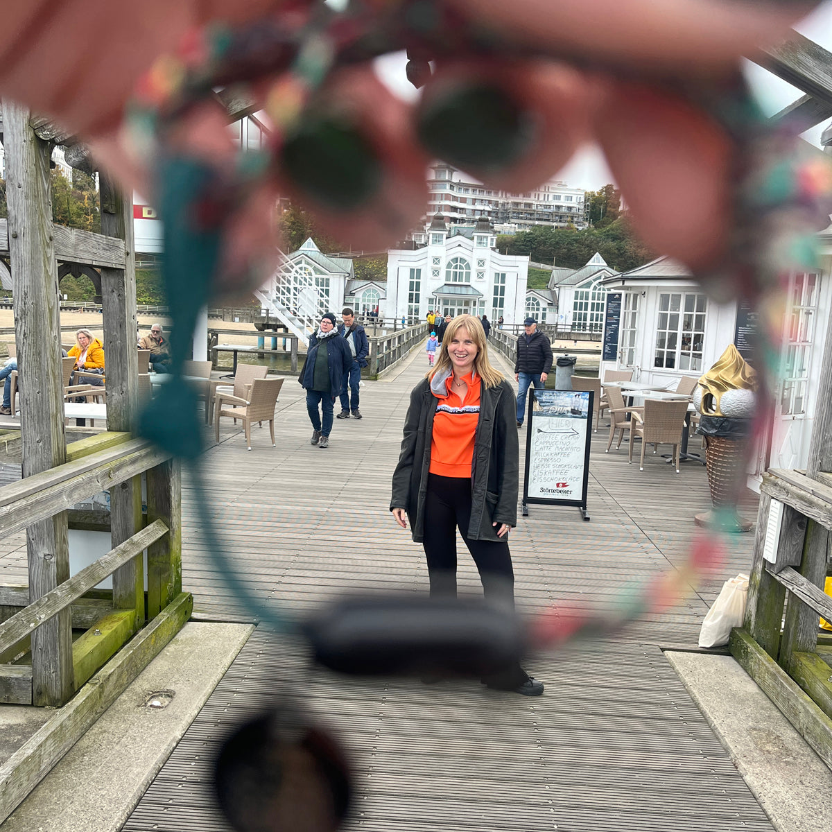 Durch das BRACENET Upcycling Armband Insel Rügen aus grünen und bunten Fischernetzen mit schwarzem Verschluss und Anhänger mit Inselgravur hindurch sieht man eine Person auf einer Seebrücke stehen.