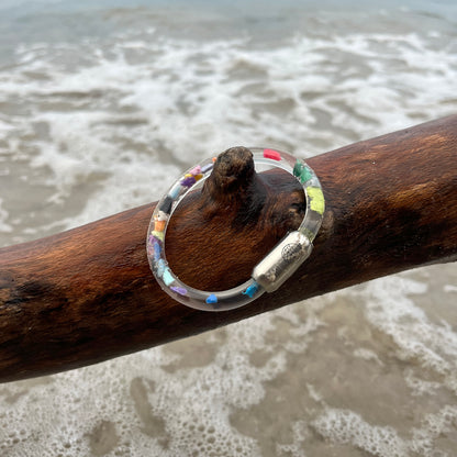 BRACENET Floating Upcycling Armband aus alten Plastiktuben gefüllt mit Mikroplastik, destilliertem Wasser und Glycerin mit magnetischem Edelstahlverschluss in silber hängt an einem Baumstamm am Meer