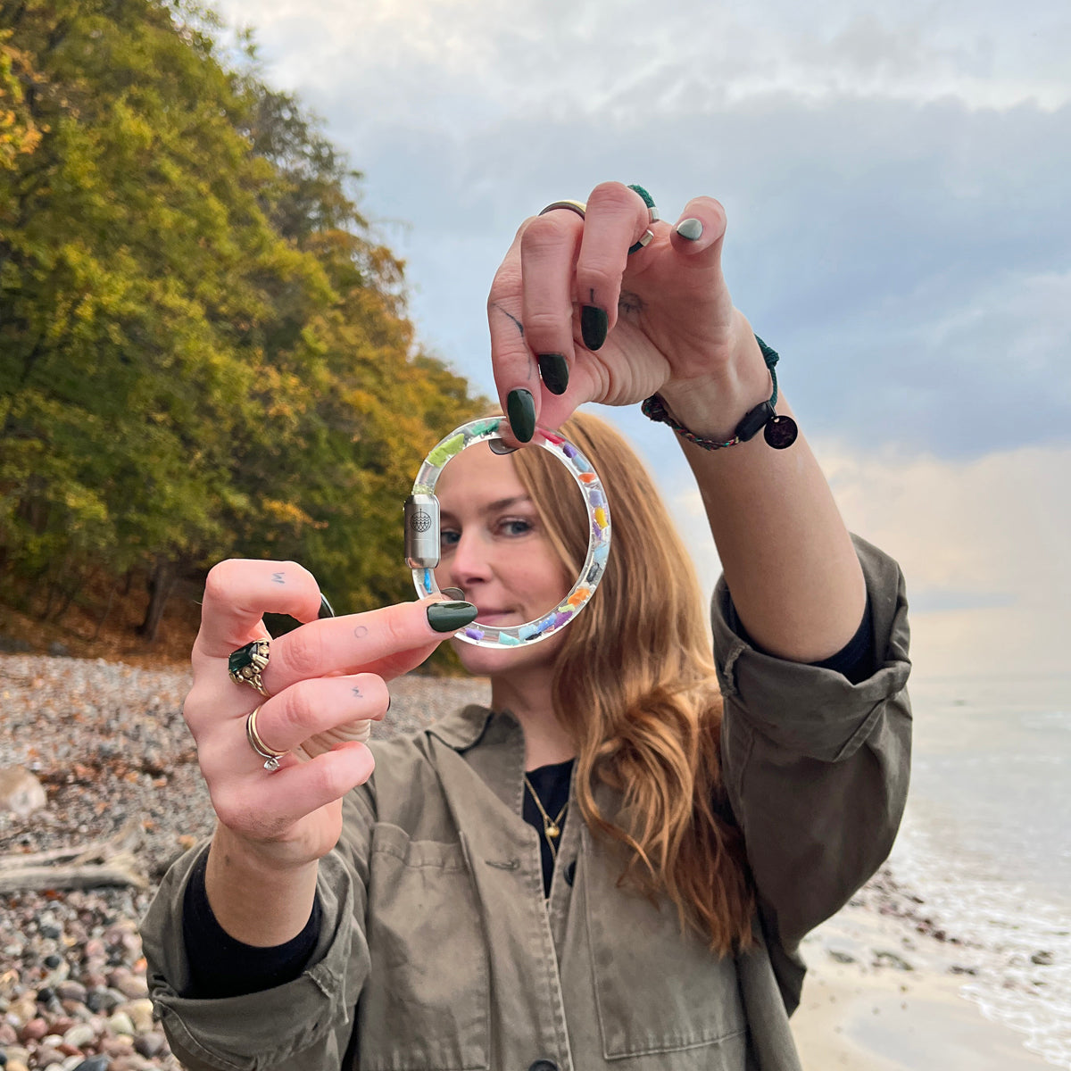 Person hält das BRACENET Floating Upcycling Armband aus alten Plastiktuben gefüllt mit Mikroplastik, destilliertem Wasser und Glycerin mit magnetischem Edelstahlverschluss in silber vor ihr Gesicht