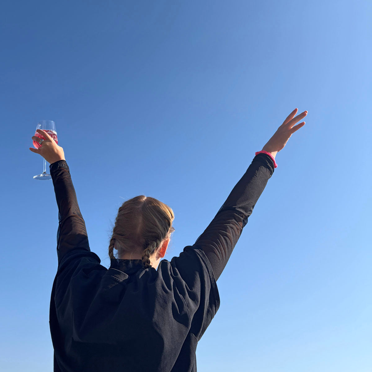Person trägt das Gulf of Bothnia Bracenet aus Fischernetz in Pink mit blauen Punkten am Handgelenk und streckt die Arme in die Luft. 