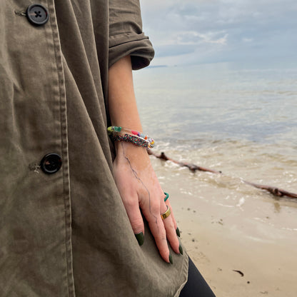 Person trägt das BRACENET Floating Upcycling Armband aus alten Plastiktuben gefüllt mit Mikroplastik, destilliertem Wasser und Glycerin mit magnetischem Edelstahlverschluss in schwarz am Handgelenk am Strand