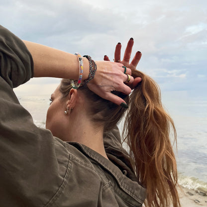 Person trägt das BRACENET Floating Upcycling Armband aus alten Plastiktuben gefüllt mit Mikroplastik, destilliertem Wasser und Glycerin mit magnetischem Edelstahlverschluss in schwarz am Handgelenk und fast sich in die Haare