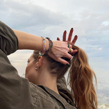 Person trägt das BRACENET Upcycling Armband Insel Rügen aus grünen und bunten Fischernetzen mit schwarzem Verschluss und Anhänger mit Inselgravur am Handgelenk und fasst sich in die Haare. 