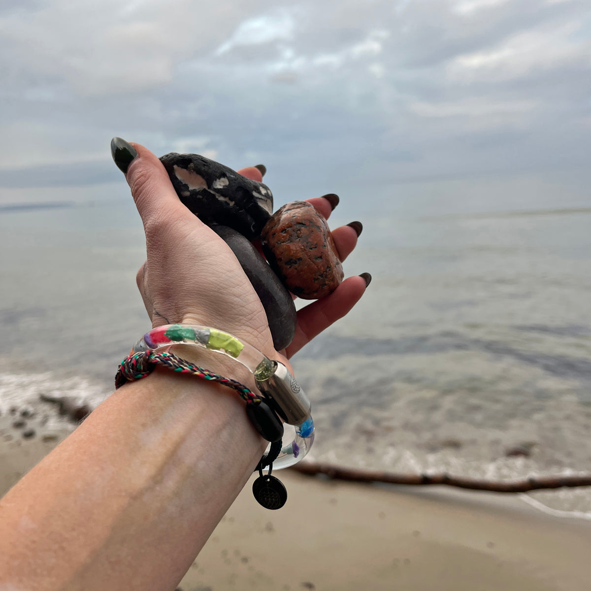 Person trägt das BRACENET Floating Upcycling Armband aus alten Plastiktuben gefüllt mit Mikroplastik, destilliertem Wasser und Glycerin mit magnetischem Edelstahlverschluss in silber am Handgelenk und hält Steine in der Hand 