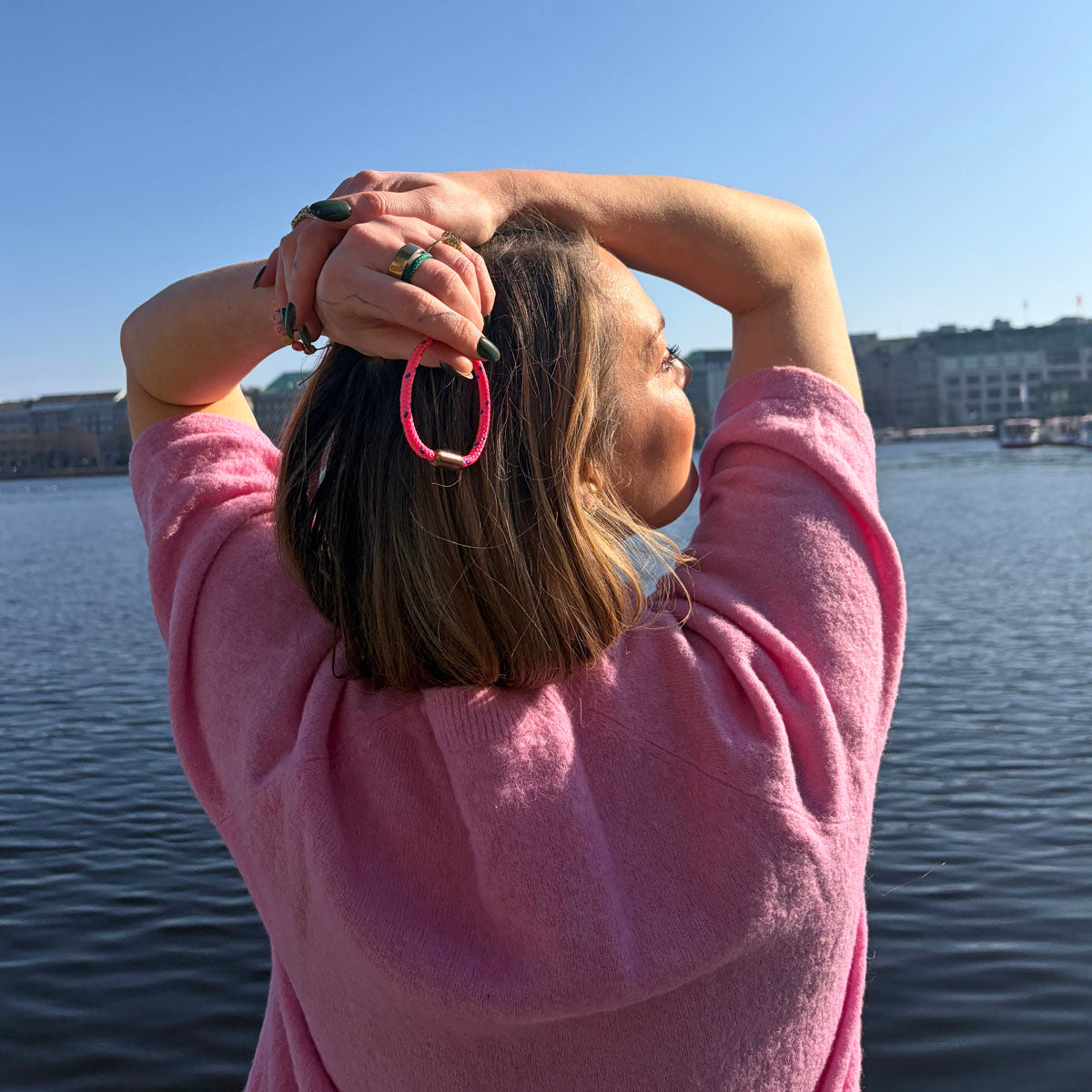 Person hält das Gulf of Bothnia Bracenet aus Fischernetz in Pink mit blauen Punkten und Magnetverschluss in Roségold in der Hand hinter dem Kopf.