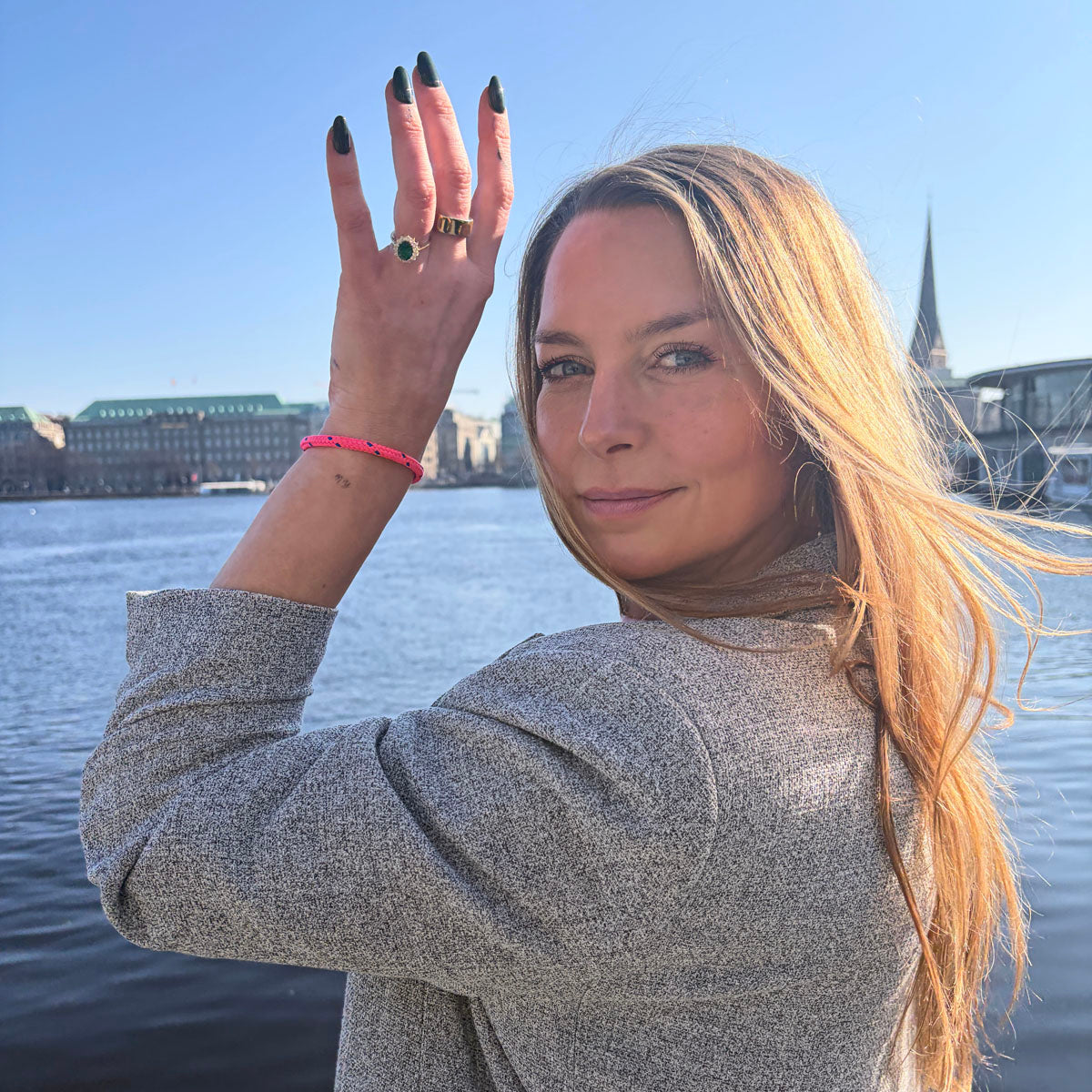 Person trägt das Gulf of Bothnia Bracenet aus Fischernetz in Pink mit blauen Punkten am Handgelenk und hält den Arm neben das Gesicht. 