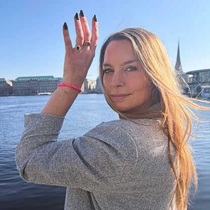 Person trägt das Gulf of Bothnia Bracenet aus Fischernetz in Pink mit blauen Punkten am Handgelenk und hält den Arm neben das Gesicht. 