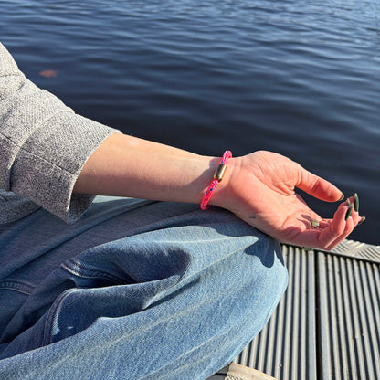 Person trägt das Gulf of Bothnia Bracenet aus Fischernetz in Pink mit blauen Punkten und Magnetverschluss in Roségold am Handgelenk und hat die Hand auf dem Bein liegen. 