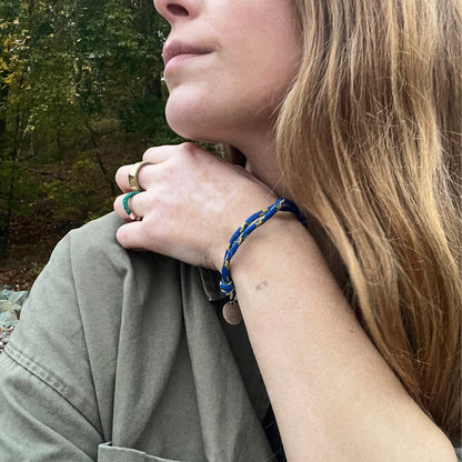 Person trägt das BRACENET Upcycling Armband Insel Sylt II aus alten Fischernetzen in dunkelblau und blau-gelb, mit einem silbernen Magnetverschluss und Anhänger mit einer Inselgravur von Sylt am Handgelenk und hat die Hand auf der Schulter liegen. 