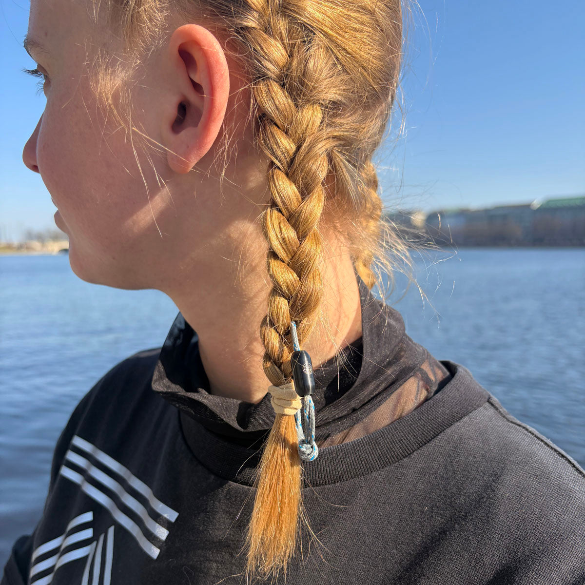 Das größenverstellbare Baltic Sea Bracenet, gefertigt aus alten Fischernetzen in Grau mit Punkten in Blau und Weiß und mit Bajonettverschluss in Schwarz hängt in den Haaren einer Person. 