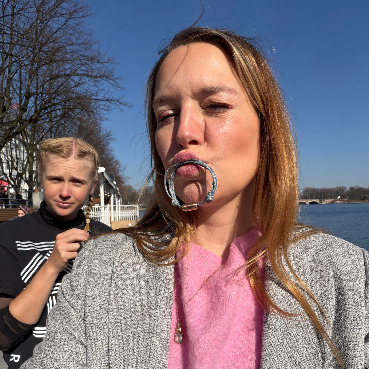 Person hat das größenverstellbare Baltic Sea Bracenet, gefertigt aus alten Fischernetzen in Grau mit Punkten in Blau und Weiß und mit Bajonettverschluss in Roségold im Mund. 
