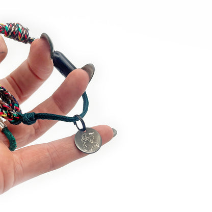 BRACENET Upcycling Armband Insel Rügen aus grünen und bunten Fischernetzen mit schwarzem Verschluss und Anhänger mit Inselgravur mit Fokus auf dem Anhänger.