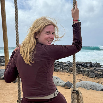 Person sitzt auf einer Schaukel am Meer und trägt das April Bracenet Gulf of Mannar aus Fischernetz in Rot und Türkis mit Knoten und mit Bajonettverschluss in Silber am Handgelenk. 