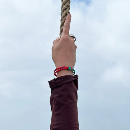 Perosn hält sich an einem Seil fest und trägt das April Bracenet Gulf of Mannar aus Fischernetz in Rot und Türkis mit Knoten und mit Bajonettverschluss in Silber am Handgelenk.