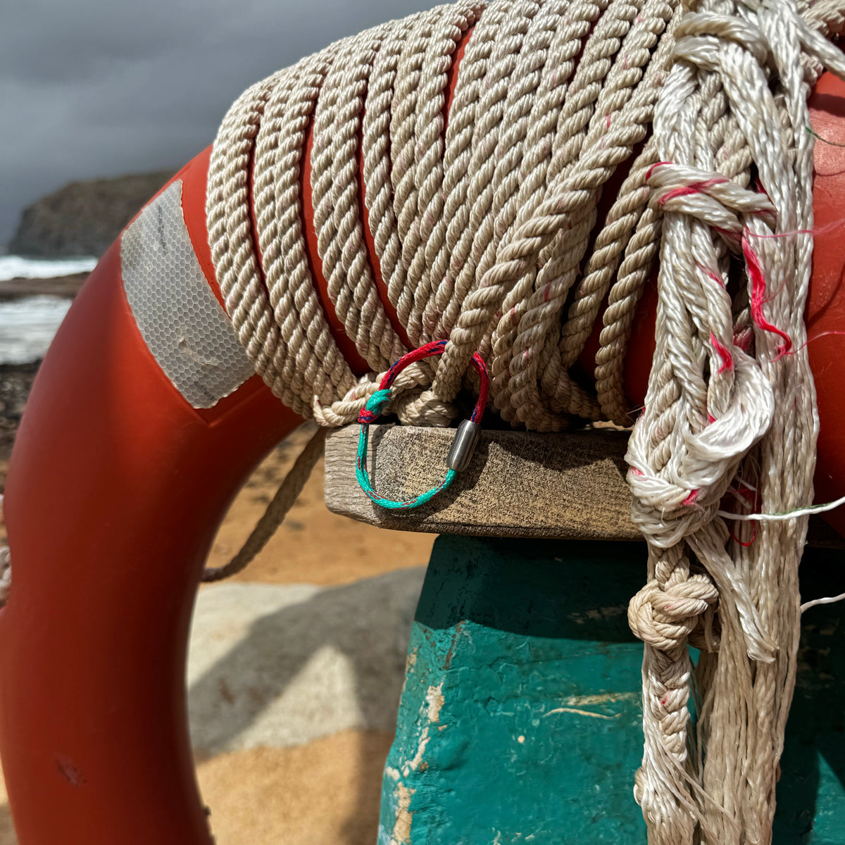 April Bracenet Gulf of Mannar aus Fischernetz in Rot und Türkis mit Knoten und mit Bajonettverschluss in Silber hängt an einem Rettungsreifen. 
