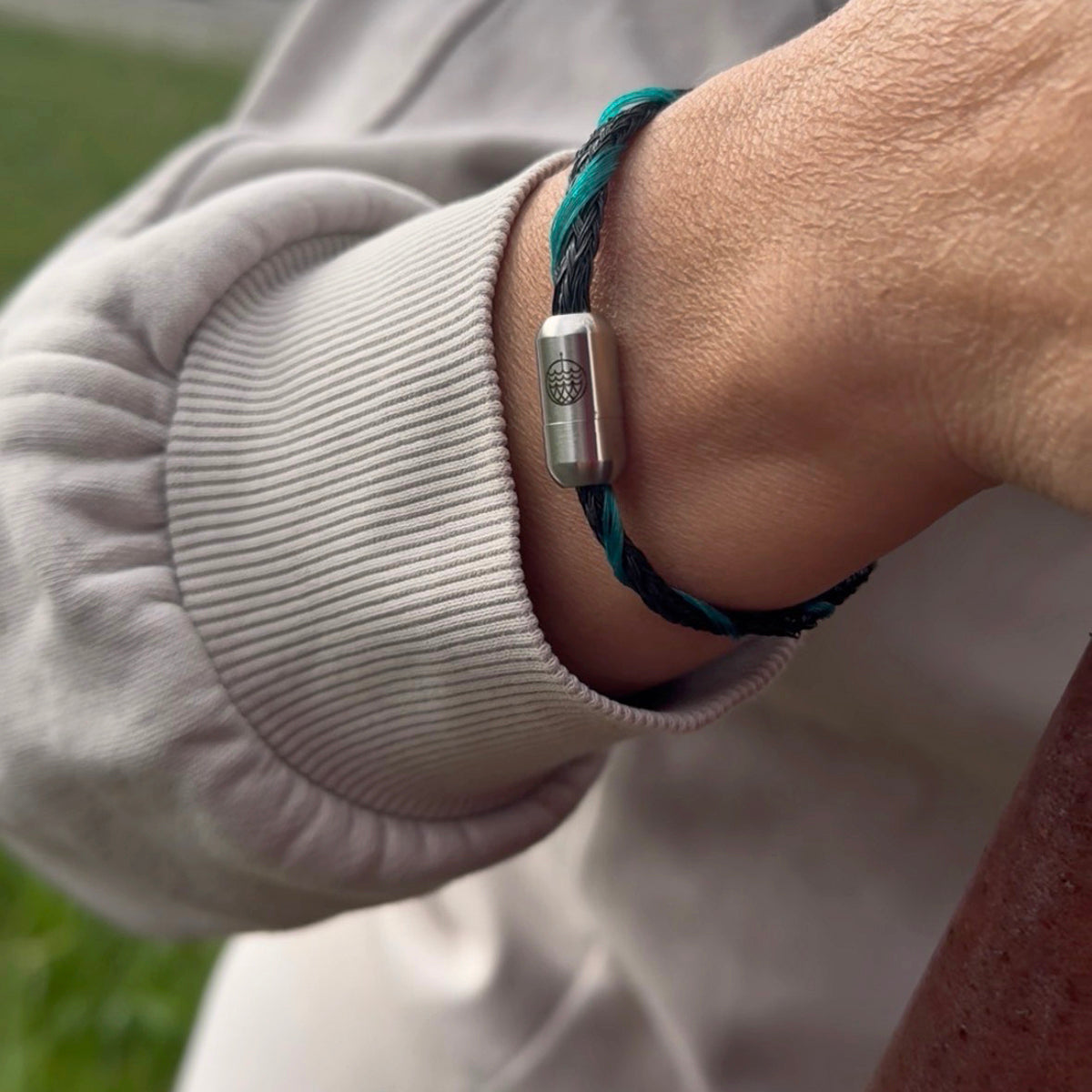 Person trägt das November BRACENET Upcycling Armband Timor Sea aus schwarzen und petrolfarbenen Fischernetzen mit silber Verschluss am Handgelenk.