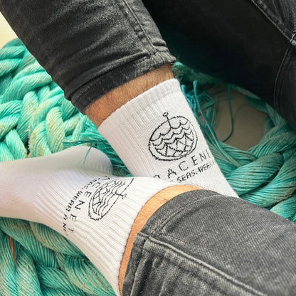 Person trägt BRACENET Baumwoll Socken in weiß mit schwarzem BRACENET Logo und sitzt auf einem alten Netz. 