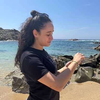 Person hat das Mai Bracenet Mayotte's Lagoon aus Fischernetz in Hellblau und Gelb mit Knoten am Handgelenk uns ist am Strand. 
