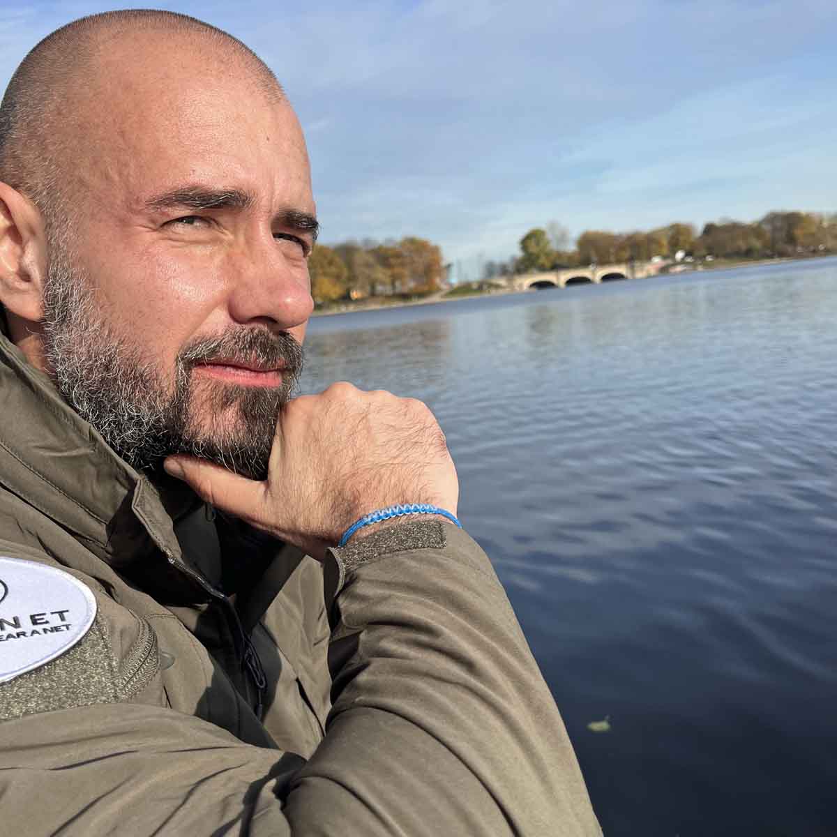 Persön tragt Dezember BRACENET Upcycling Armband Arctic Ocean II aus blauen Fischernetzen mit Makramee Knoten in Hellblau und Magnetverschluss aus Edelstahl in Silber am Handgelenk und schaut in die Ferne. 