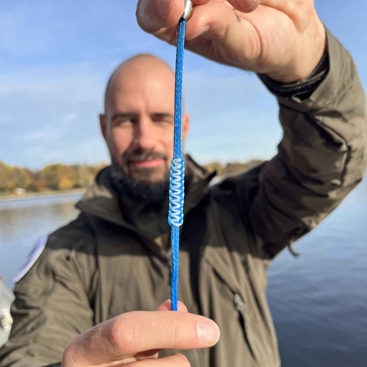 Person hält das Dezember BRACENET Upcycling Armband Arctic Ocean II aus blauen Fischernetzen mit Makramee Knoten in Hellblau und Magnetverschluss aus Edelstahl in Silber lang gestreckt vor sich und lächelt. 