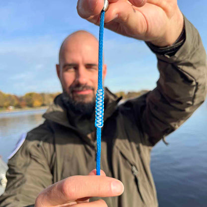 Person hält das Dezember BRACENET Upcycling Armband Arctic Ocean II aus blauen Fischernetzen mit Makramee Knoten in Hellblau und Magnetverschluss aus Edelstahl in Silber lang gestreckt vor sich und lächelt. 