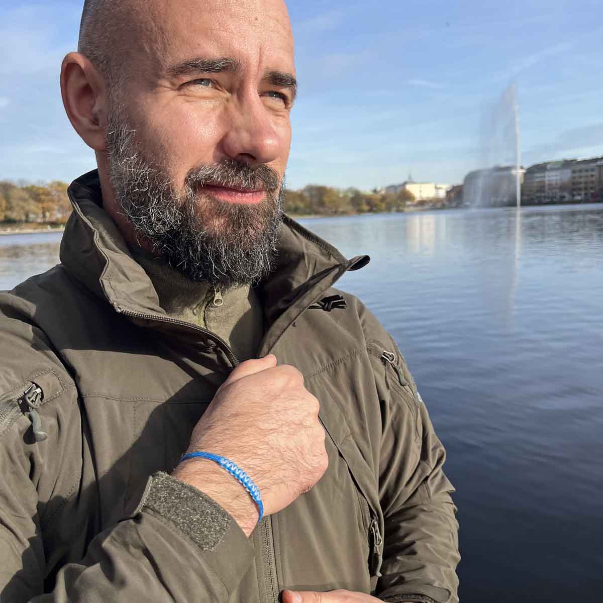 Person trägt das Dezember BRACENET Upcycling Armband Arctic Ocean II aus blauen Fischernetzen mit Makramee Knoten in Hellblau und Magnetverschluss aus Edelstahl in Silber am Handgelenk und schließt seine Jacke. 