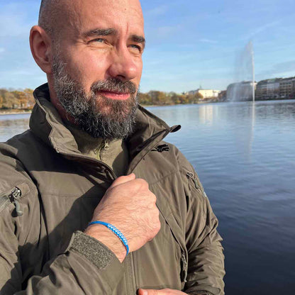 Person trägt das Dezember BRACENET Upcycling Armband Arctic Ocean II aus blauen Fischernetzen mit Makramee Knoten in Hellblau und Magnetverschluss aus Edelstahl in Silber am Handgelenk und schließt seine Jacke. 