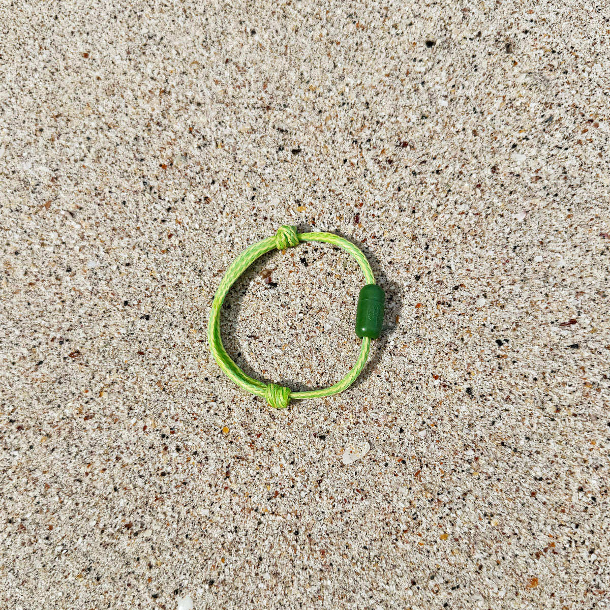 Juni Bracenet Bismarck Sea aus Fischernetz in Hellgrün mit Magnetverschluss aus eingeschmolzenen Fischernetzen in Grün liegt im Sand. 