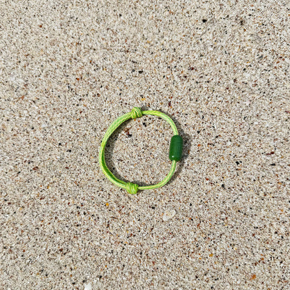 Juni Bracenet Bismarck Sea aus Fischernetz in Hellgrün mit Magnetverschluss aus eingeschmolzenen Fischernetzen in Grün liegt im Sand. 