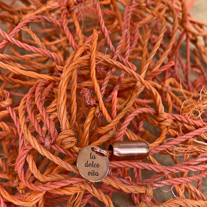 La Dolce Vita Toskana Bracenet Bracelet aus Fischernetz in orange mit Edelstahl Magnetverschluss und einem Edelstahlanhänger mit La Dolce Vita Gravur mit Fischernetzen im Hintergrund