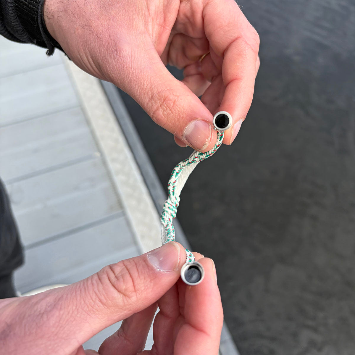 Person öffnet das Enard Bay Bracenet aus Fischernetz in Weiß und Grün mit Umwicklung in der Mitte und mit Bajonettverschluss in Silber. 