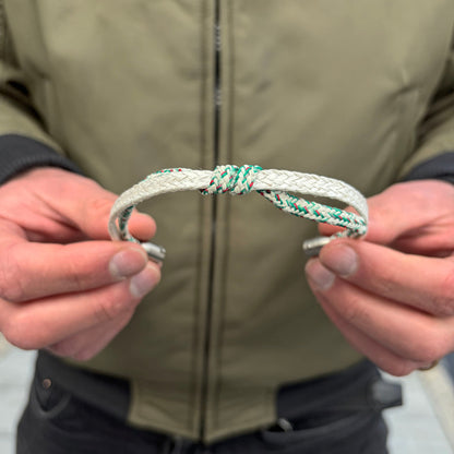 Person hält das geöffnete Enard Bay Bracenet aus Fischernetz in Weiß und Grün mit Umwicklung in der Mitte und mit Bajonettverschluss in Silber in den Händen. 