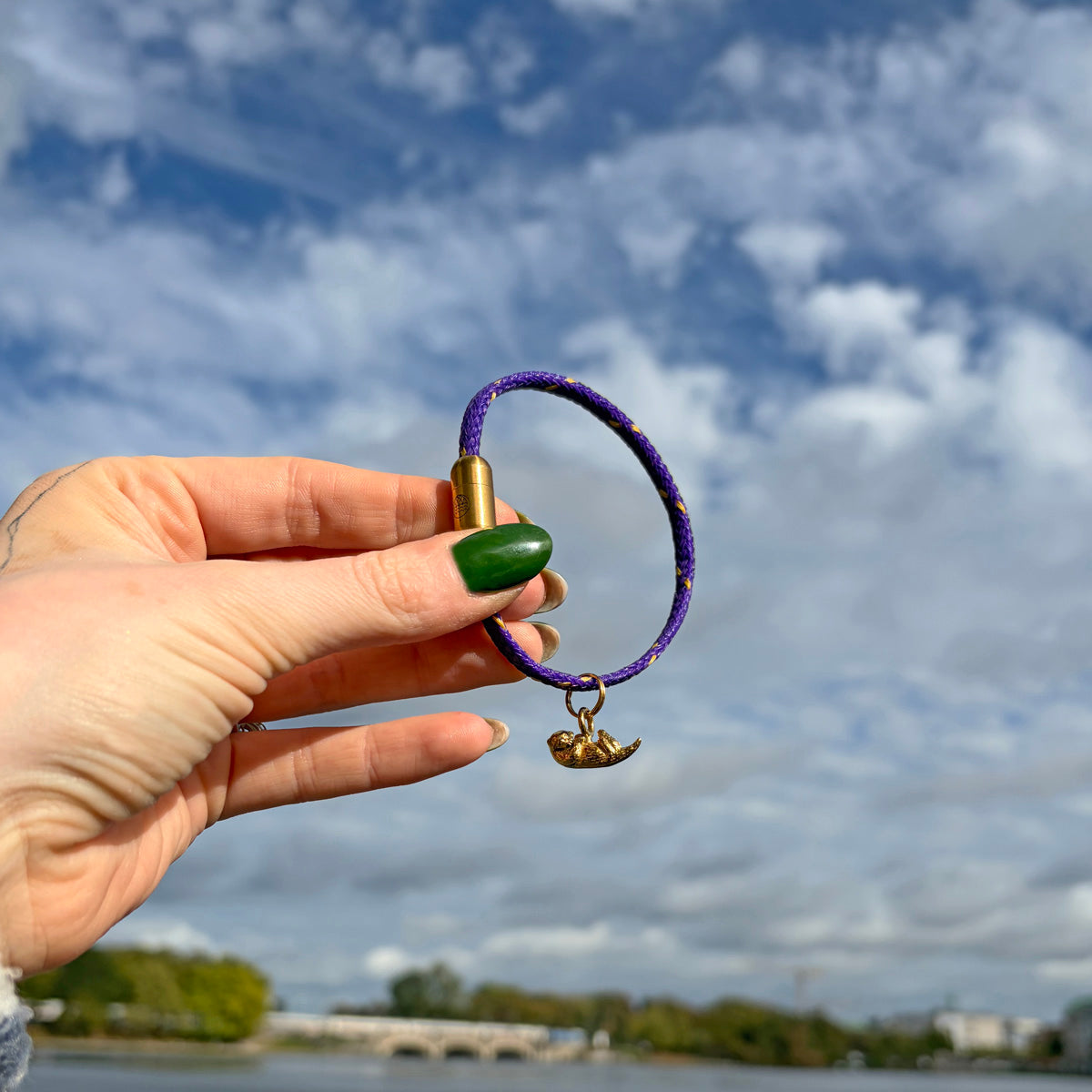 Person hält das BRACENET Armband aus Fischernetz in Lila mit Magnetverschluss in Roségold und einem Otter-Anhänger in Roségold zwischen den Fingern.