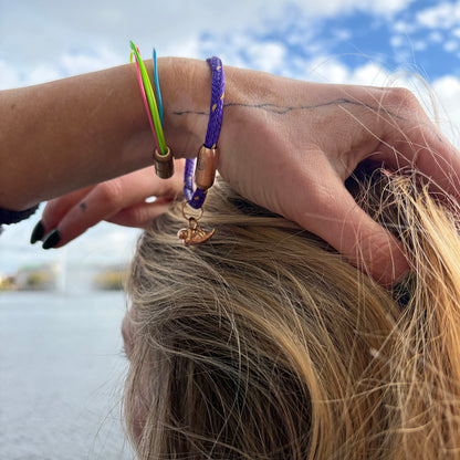 Person trägt das BRACENET Armband aus Fischernetz in Lila mit Magnetverschluss in Roségold und einem Otter-Anhänger in Roségold am Handgelenk und fasst sich in die Haare.