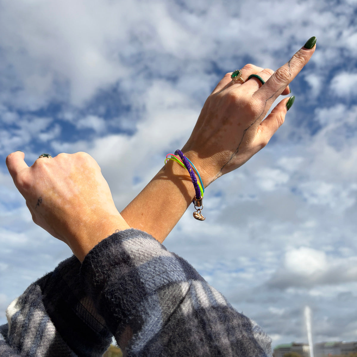 Person zeigt in den Himmel und trägt das BRACENET Armband aus Fischernetz in Lila mit Magnetverschluss in Roségold und einem Otter-Anhänger in Roségold am Handgelenk. 