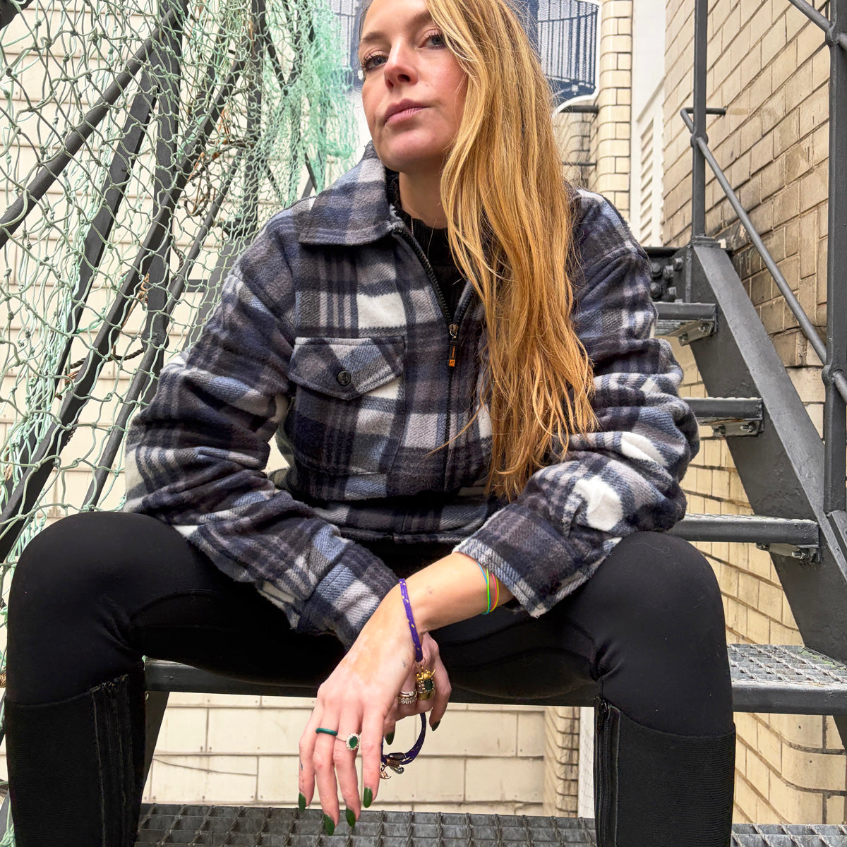 Person sitzt auf einer Treppe und trägt das BRACENET Armband aus Fischernetz in Lila mit Magnetverschluss in Gold und einem Otter-Anhänger in Gold am Handgelenk. 