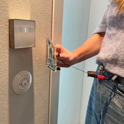 Person nutzt den BRACENET Karten- und Schlüsselhalter mit ausziehbarer Zugrolle, BRACENET Logo, Schnürung aus Red Sea Fischernetz und schwarzem Karabiner um eine Hotel Tür mit der Karte zu öffnen. Der Schlüssel- und Kartenhalter ist am Hosenbund befestigt. 