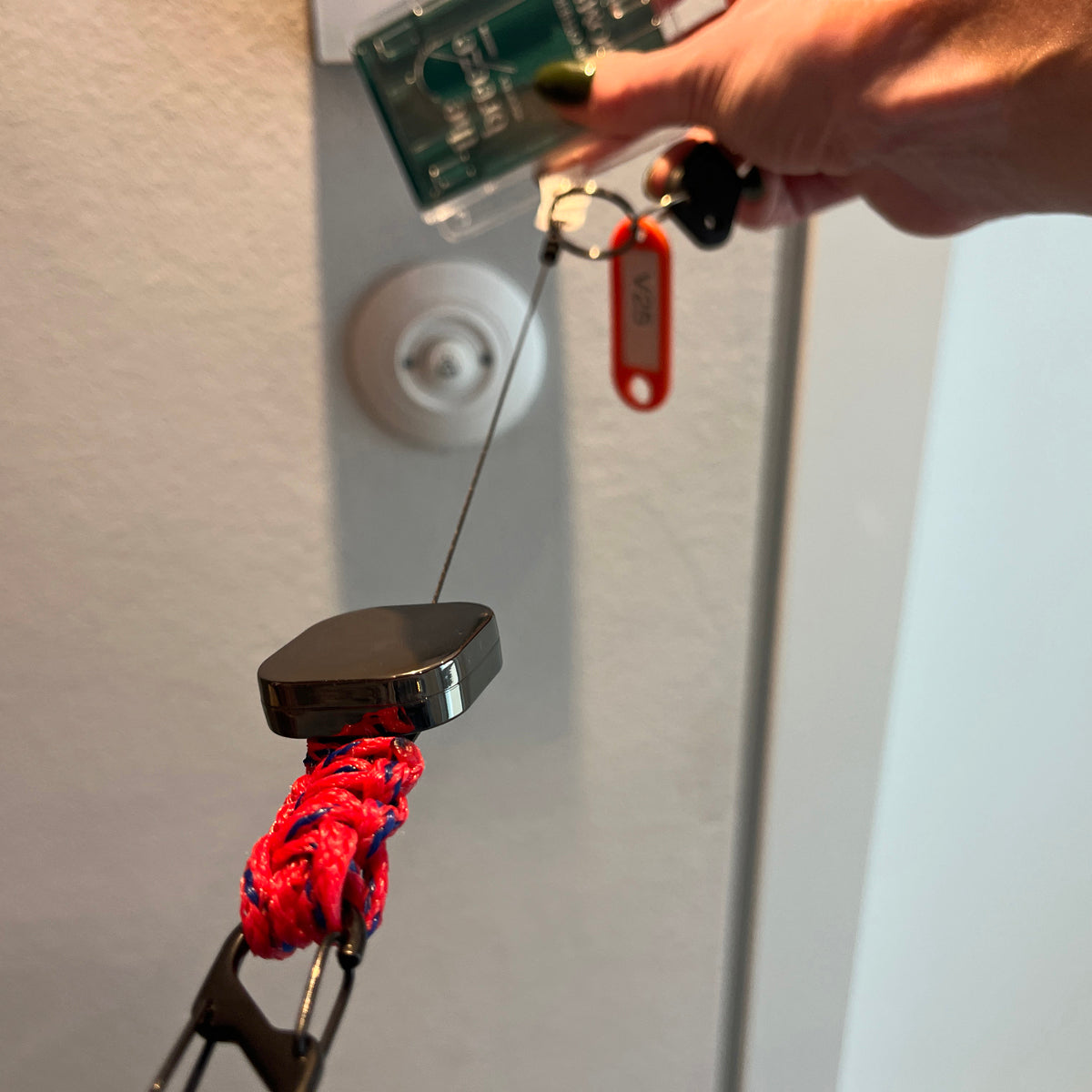 Person nutzt den BRACENET Karten- und Schlüsselhalter mit ausziehbarer Zugrolle, BRACENET Logo, Schnürung aus Red Sea Fischernetz und schwarzem Karabiner um eine Tür zu öffnen. 