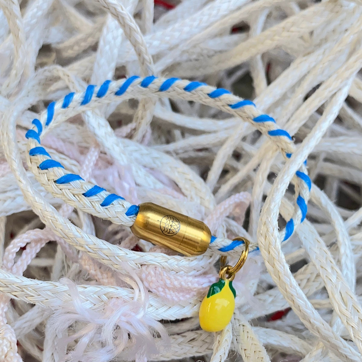 Almalfi Bracenet Bracelet aus Fischernetz in weiß und blau mit Edelstahl Magnetverschluss und einem Zitronenanhänger mit Netz im Hintergrund